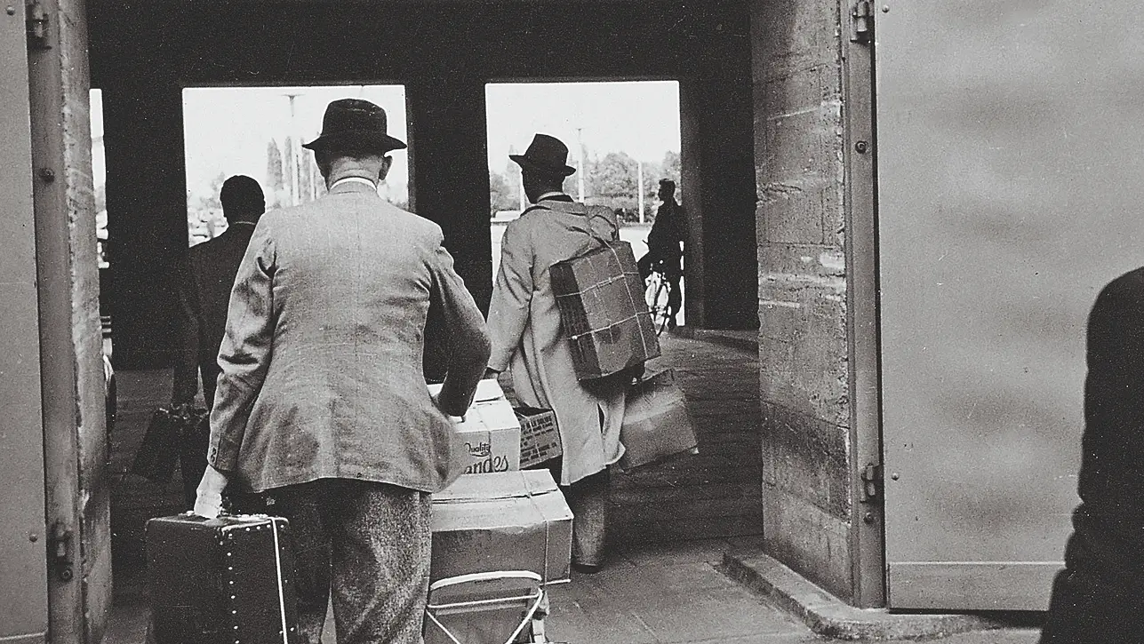 Schwarz-weiß Foto von Käthe und Wilhelm Wohlfahrt beim Tragen von Geschenken durch eine Tür in den 1960er Jahren